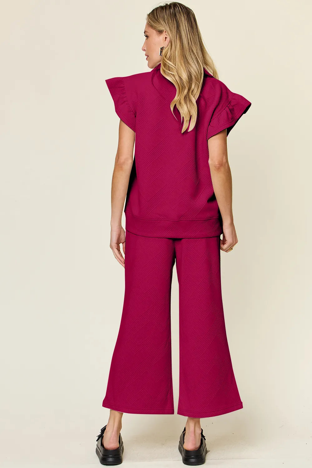 Rear view of a woman modeling a textured ruffle short sleeve top and wide leg pants set in maroon.