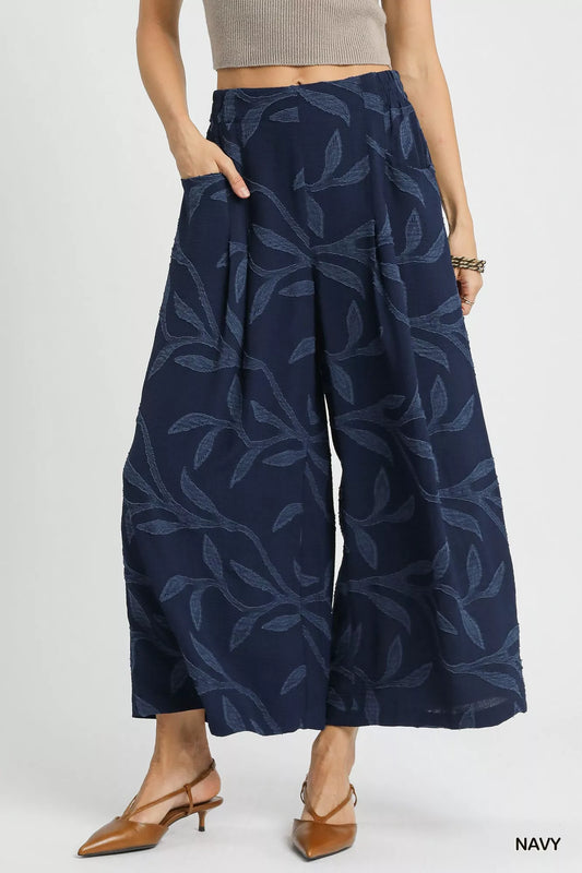 Navy jacquard wide-leg pants with leaf pattern and side pockets, modeled on a woman.