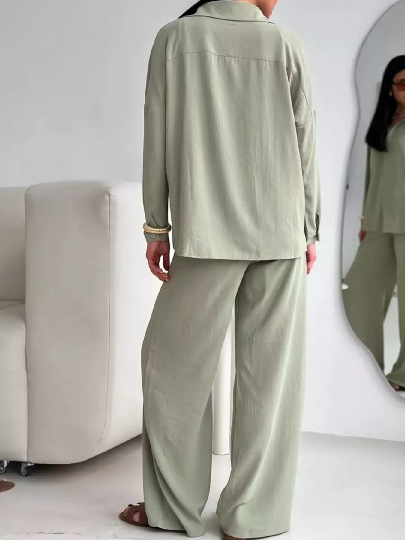 Woman wearing a sage green two-piece button-down shirt and wide-leg pants set, viewed from behind.