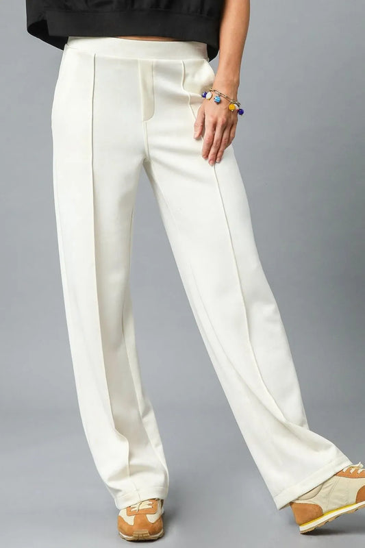 Cream high-waisted wide-leg pants in linen blend, modeled on a woman with bracelets and sneakers.