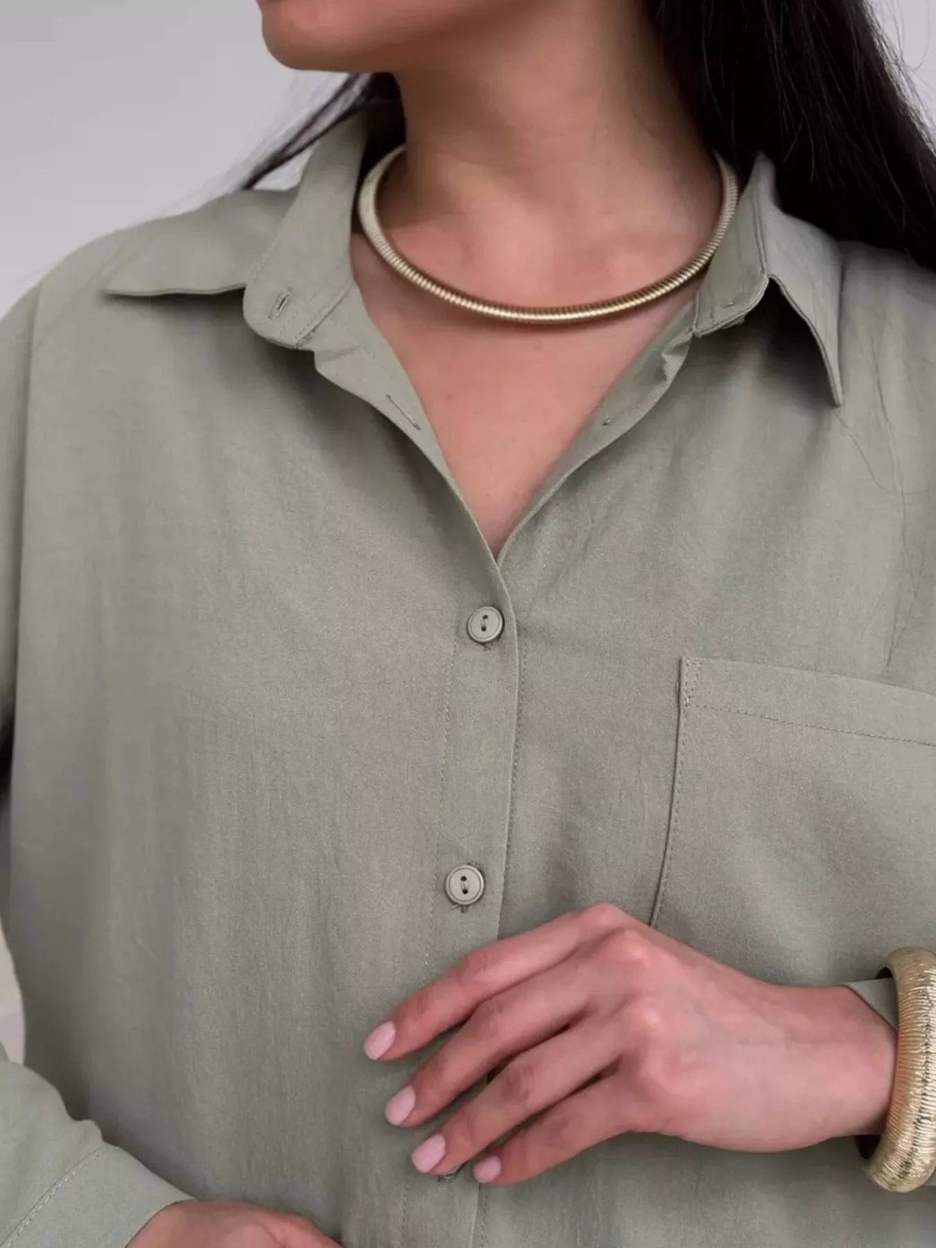 Close-up of a woman wearing a light green button-down shirt with a gold choker necklace and bracelet.