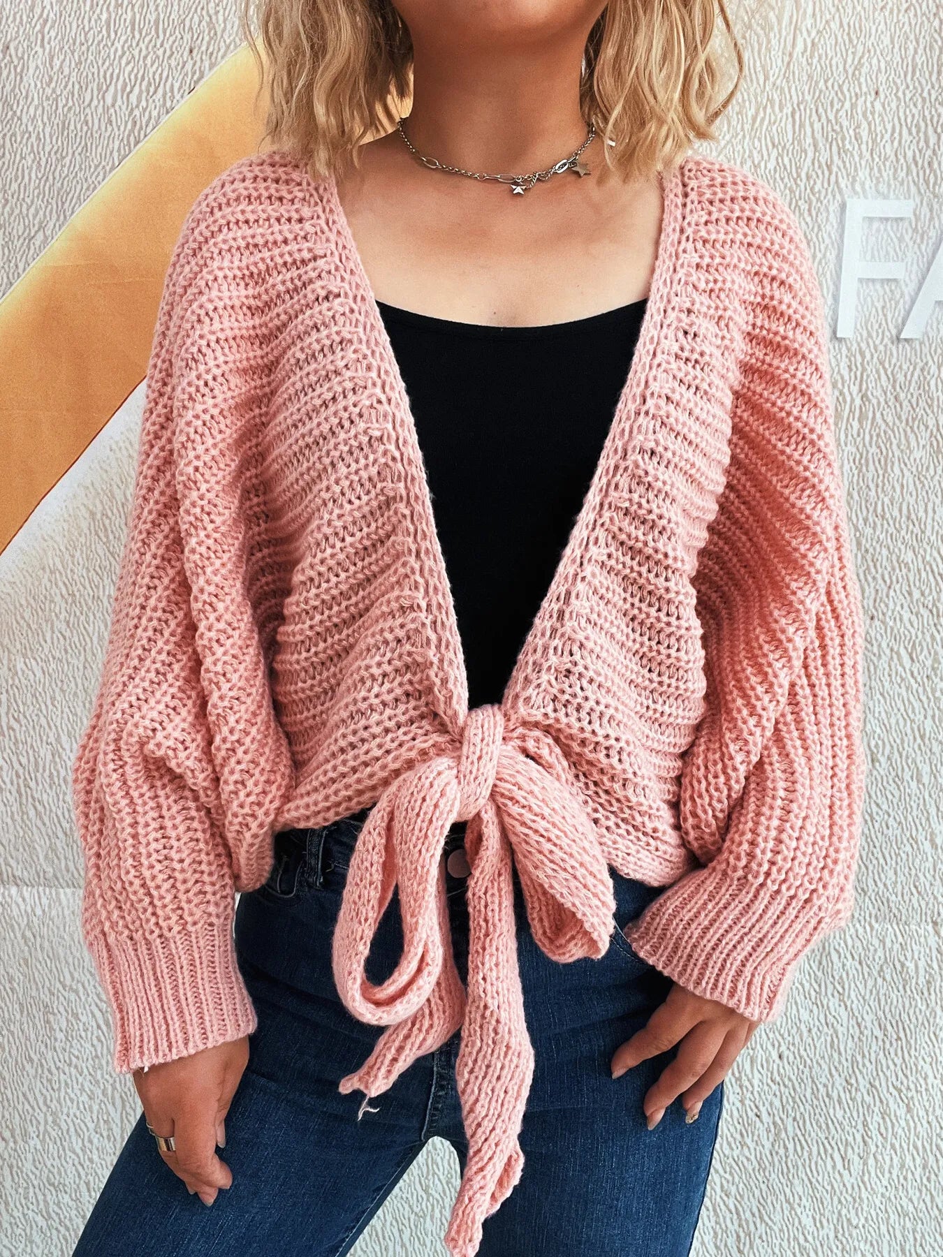 Woman wearing a light blue tie-front long-sleeve knit cardigan over a black top and jeans.