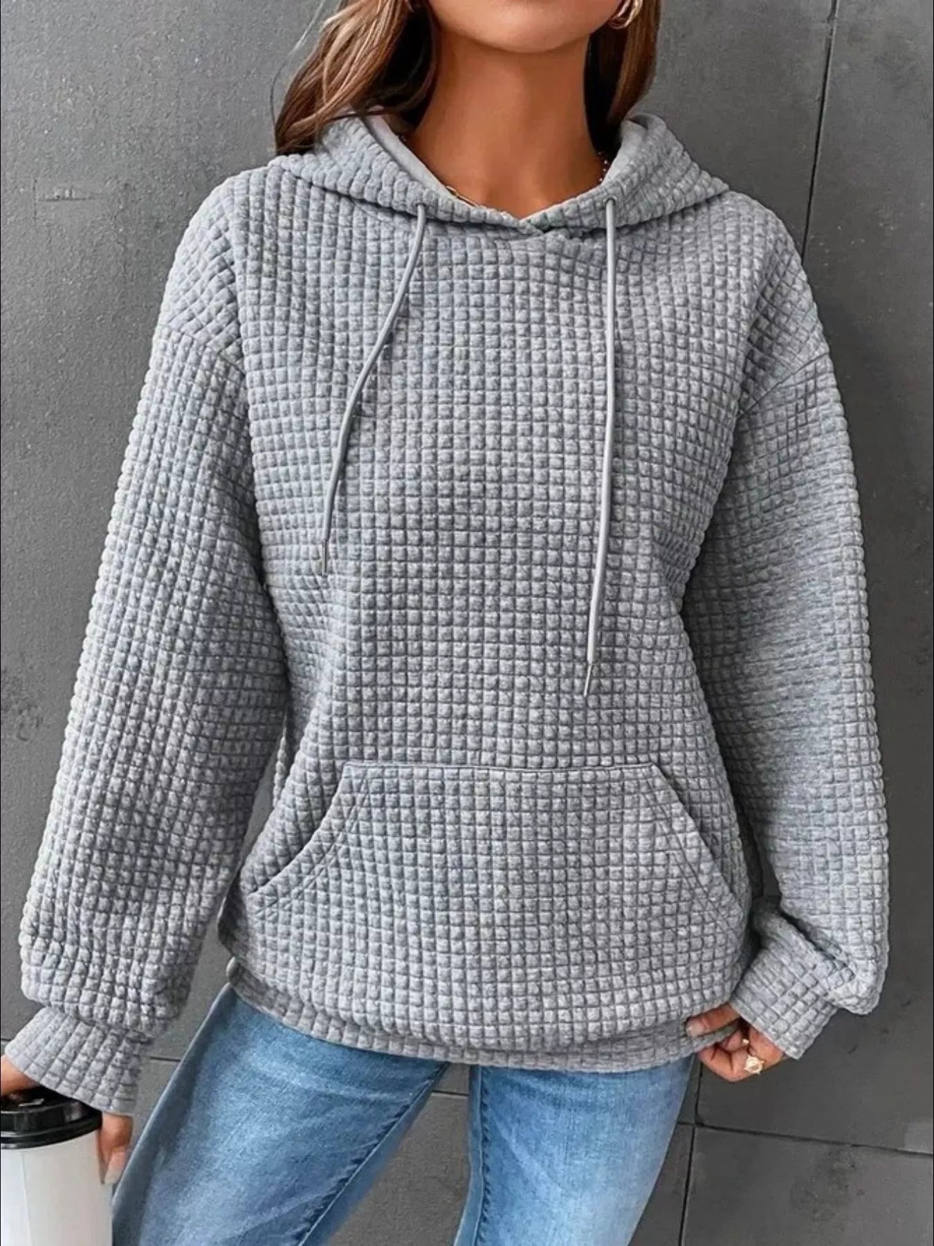 Gray waffle knit hoodie with drawstring hood and front pocket, modeled on a woman.