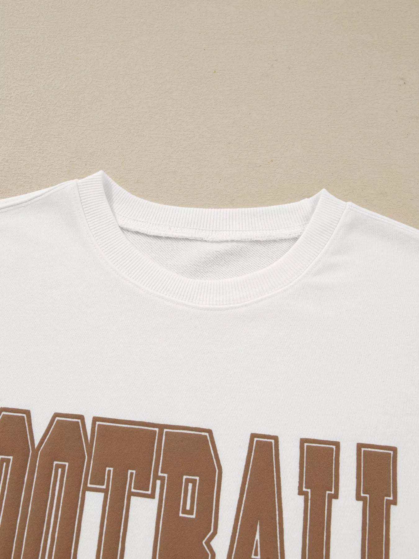 White crew neck sweatshirt with brown 3D football graphic.
