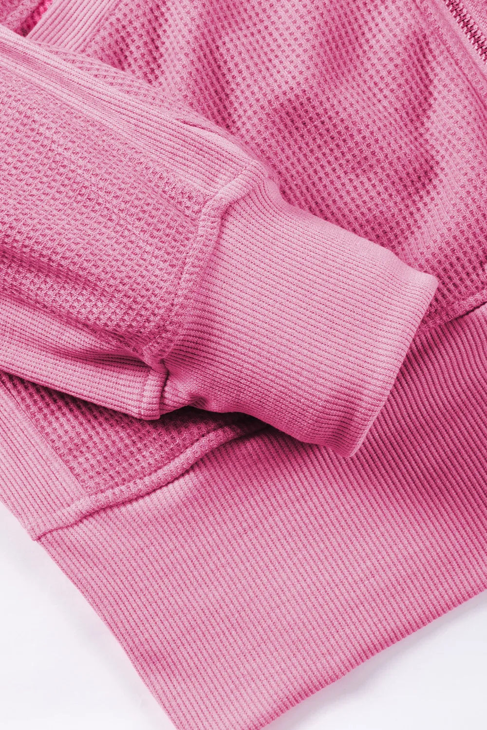 Pink waffle-knit zip-up hooded jacket with long sleeves and cuffs.