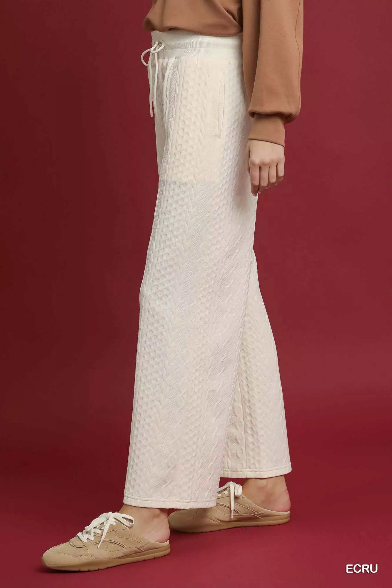 White cable knit textured wide leg pants with drawstring waist, modeled on a red background.