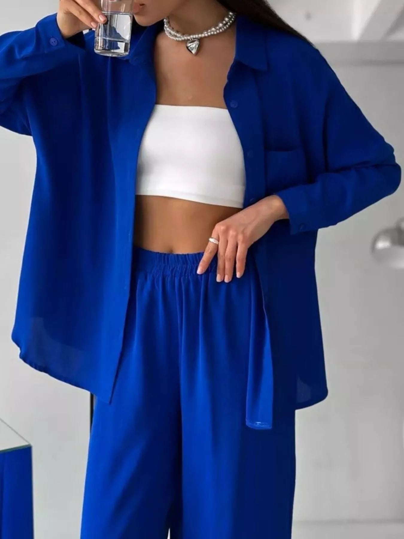 Woman wearing a blue two-piece set with button-down shirt and wide-leg pants, layered over a white tube top.