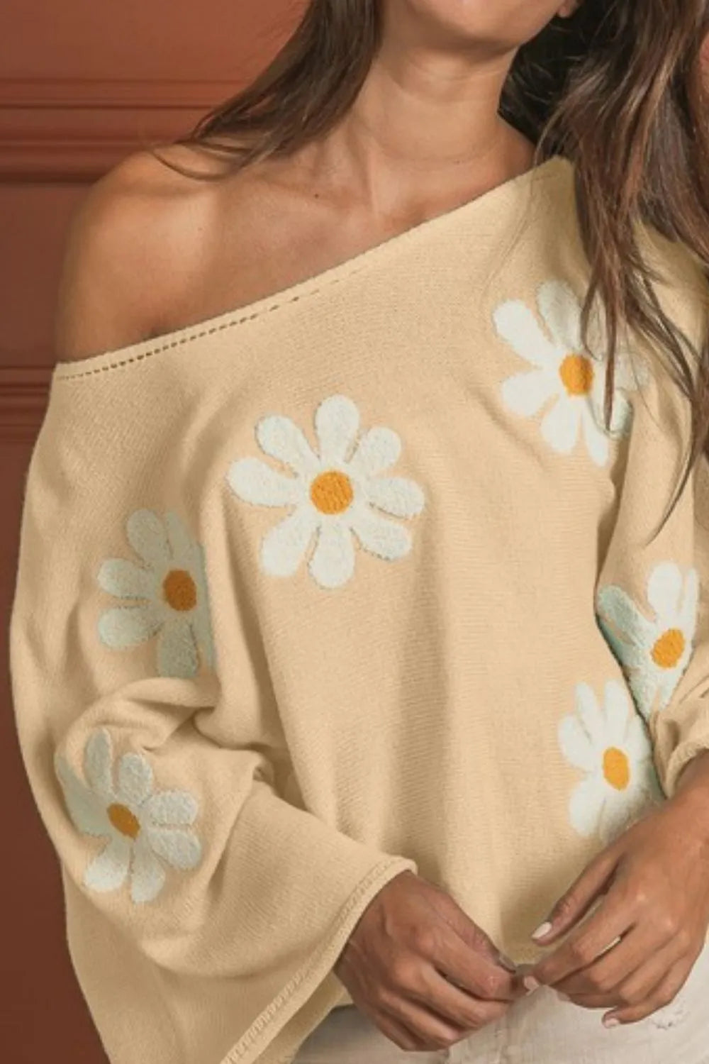 Loose fit knit top in beige with embroidered white daisy flowers and off-shoulder neckline.