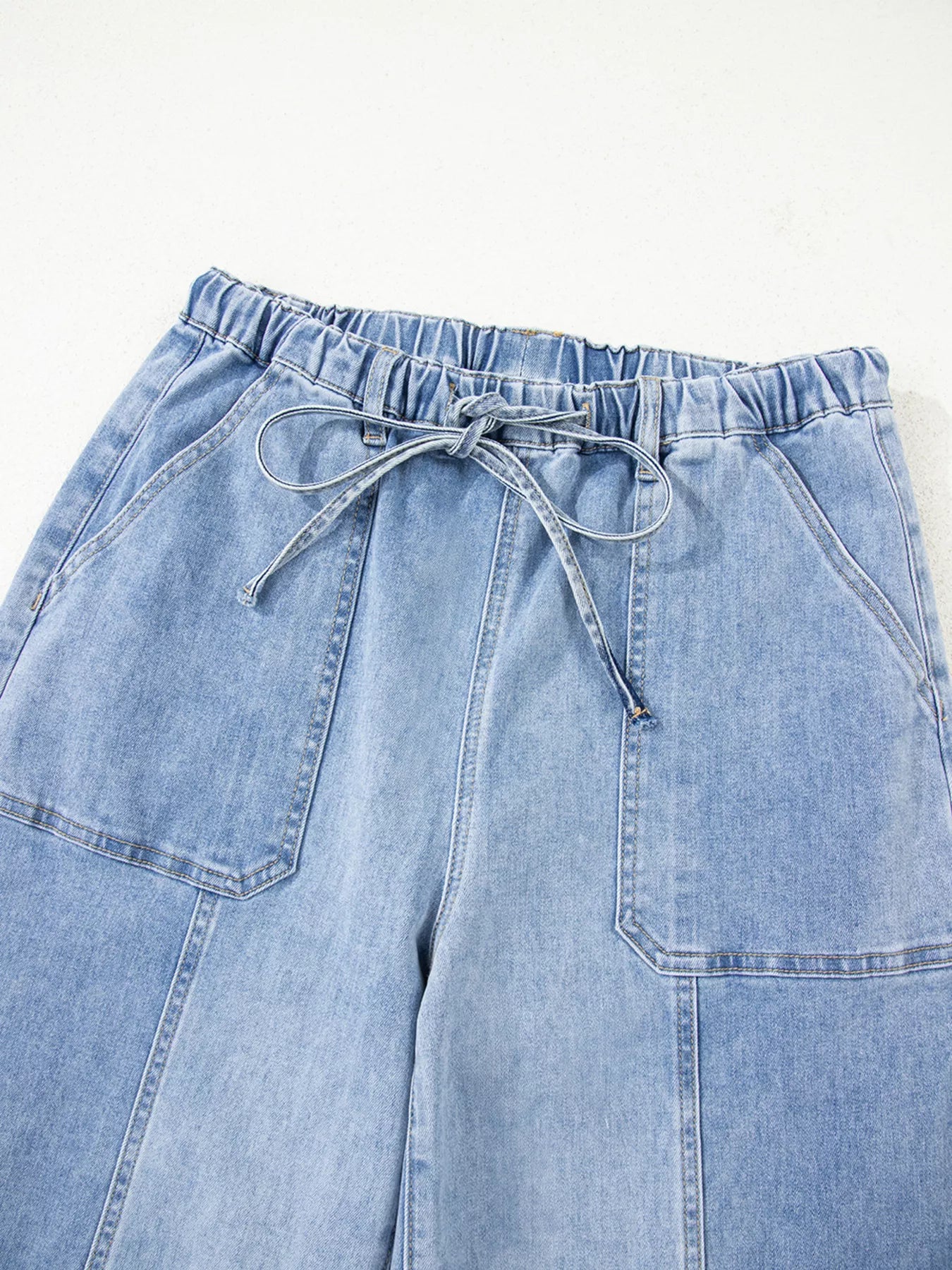 Light wash wide-leg jeans with drawstring waist and raw hem.