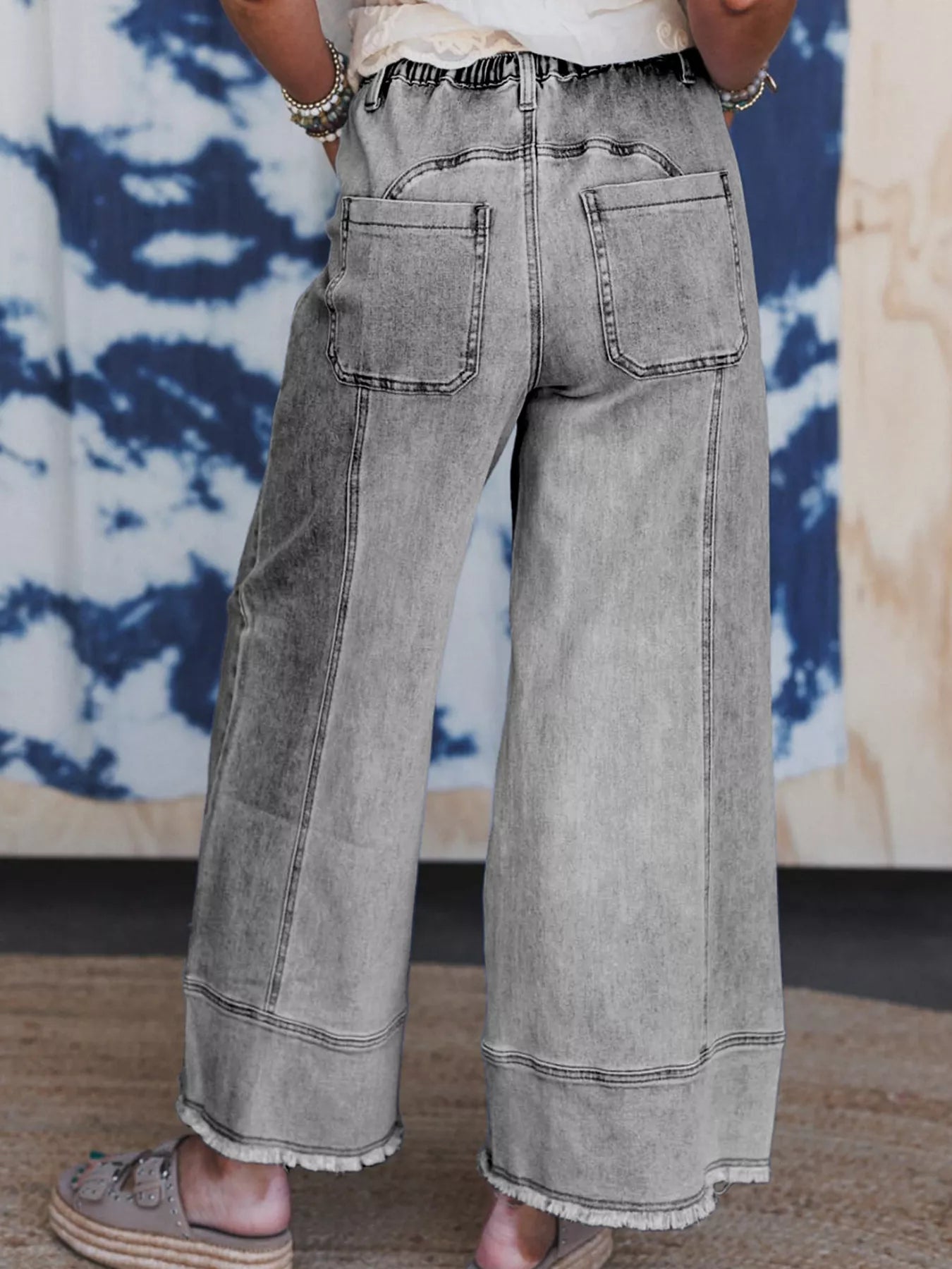 Rear view of light wash wide-leg drawstring jeans with raw hem and pockets.