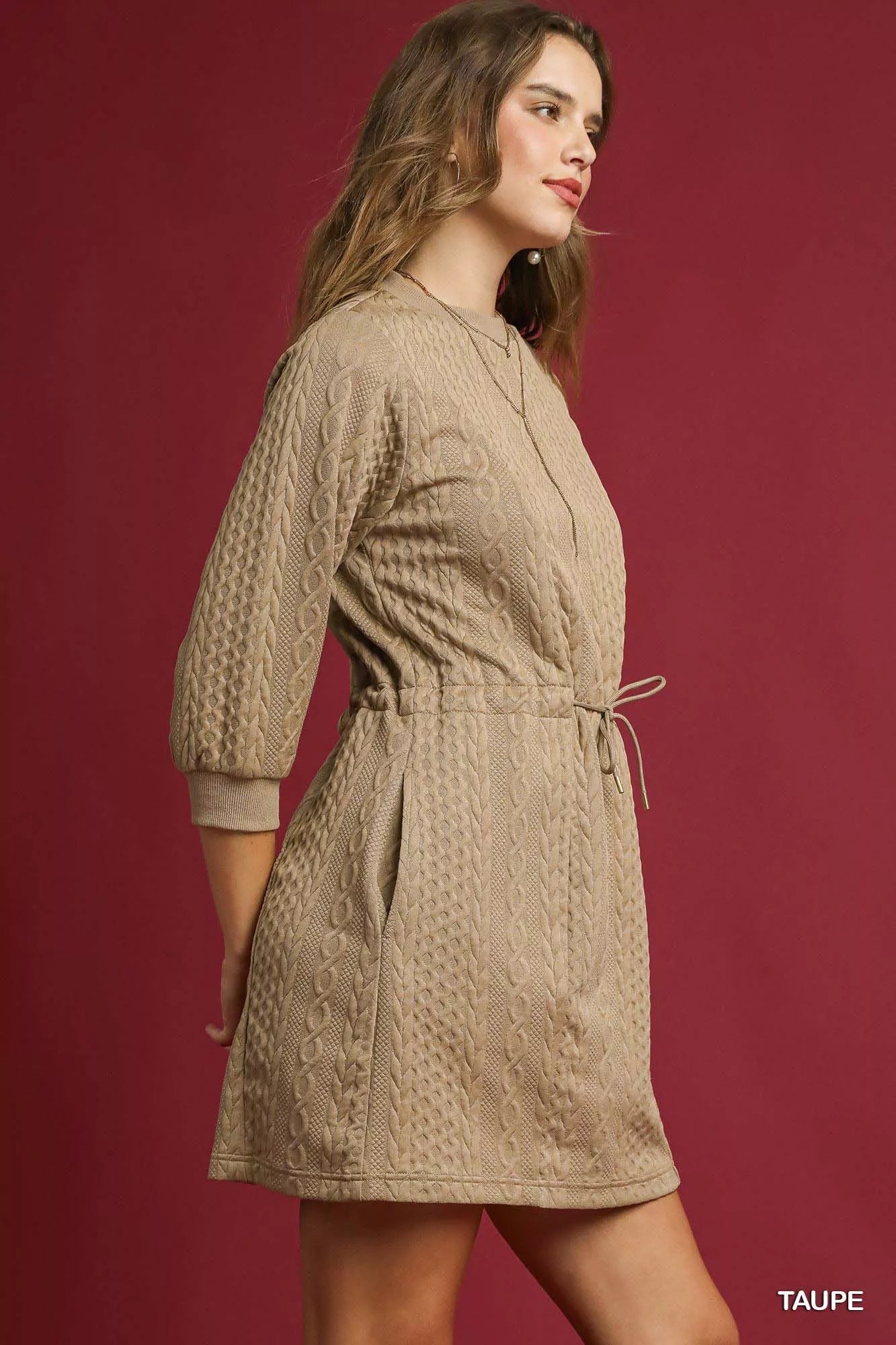 Side view of a model wearing a tan cable knit mini dress with drawstring waist and pockets.