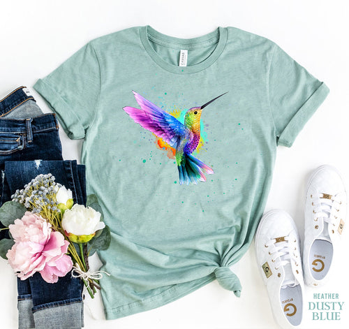Light green unisex cotton t-shirt with a colorful watercolor hummingbird design, styled with jeans and white sneakers.