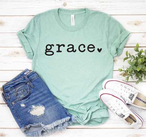 Light green unisex t-shirt with black "grace" text, styled with jeans and sneakers on a wooden surface.
