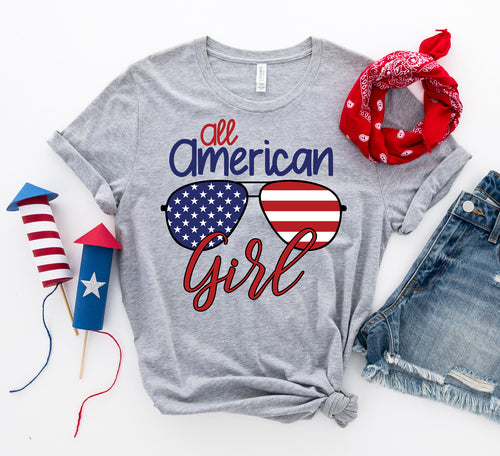 Gray Bella Canvas cotton t-shirt with "All American Girl" text and American flag sunglasses graphic, styled with red bandana and fireworks.