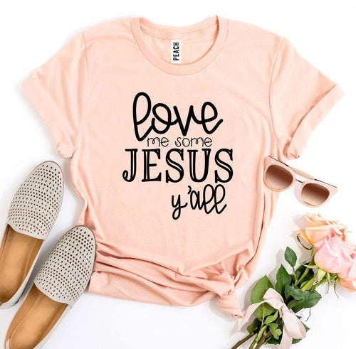 Pink Bella Canvas cotton T-shirt with "Love Me Some Jesus Y'all" text, styled with espadrilles, sunglasses, and roses.