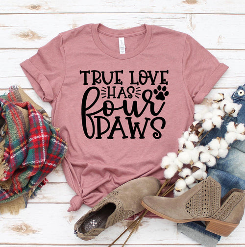 Pink Bella Canvas T-shirt with "True Love Has 4 Paws" text and paw print design, laid flat on wood with plaid scarf, jeans, and tan shoes.