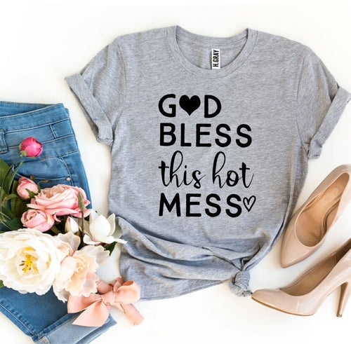 Gray Bella Canvas cotton T-shirt with "God Bless this Hot Mess" text and heart graphics, styled with jeans and heels.