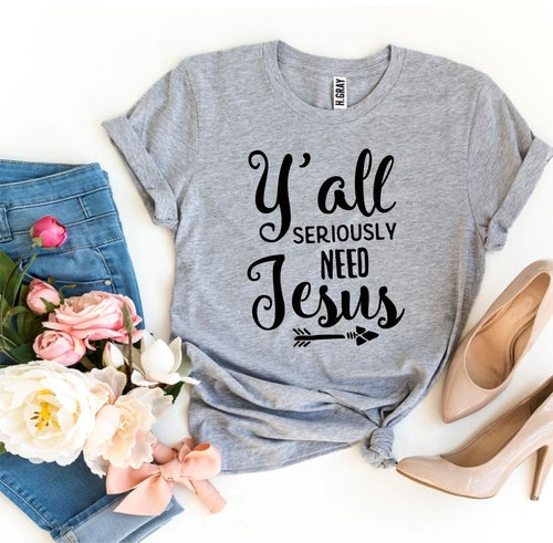 Gray Bella Canvas cotton t-shirt with "Y'all Seriously Need Jesus" text, styled with jeans, pink roses, and nude heels.