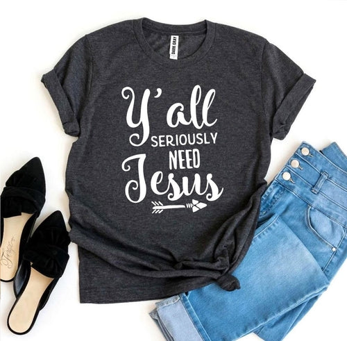 Heather gray Bella Canvas cotton T-shirt with "Y'all Seriously Need Jesus" text and arrows, styled with jeans and black heels.