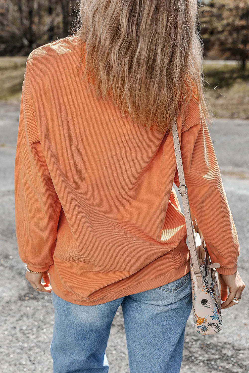 Rear view of a woman wearing an orange long-sleeve polyester sweatshirt with letter graphic, paired with jeans and a crossbody bag, outdoors.