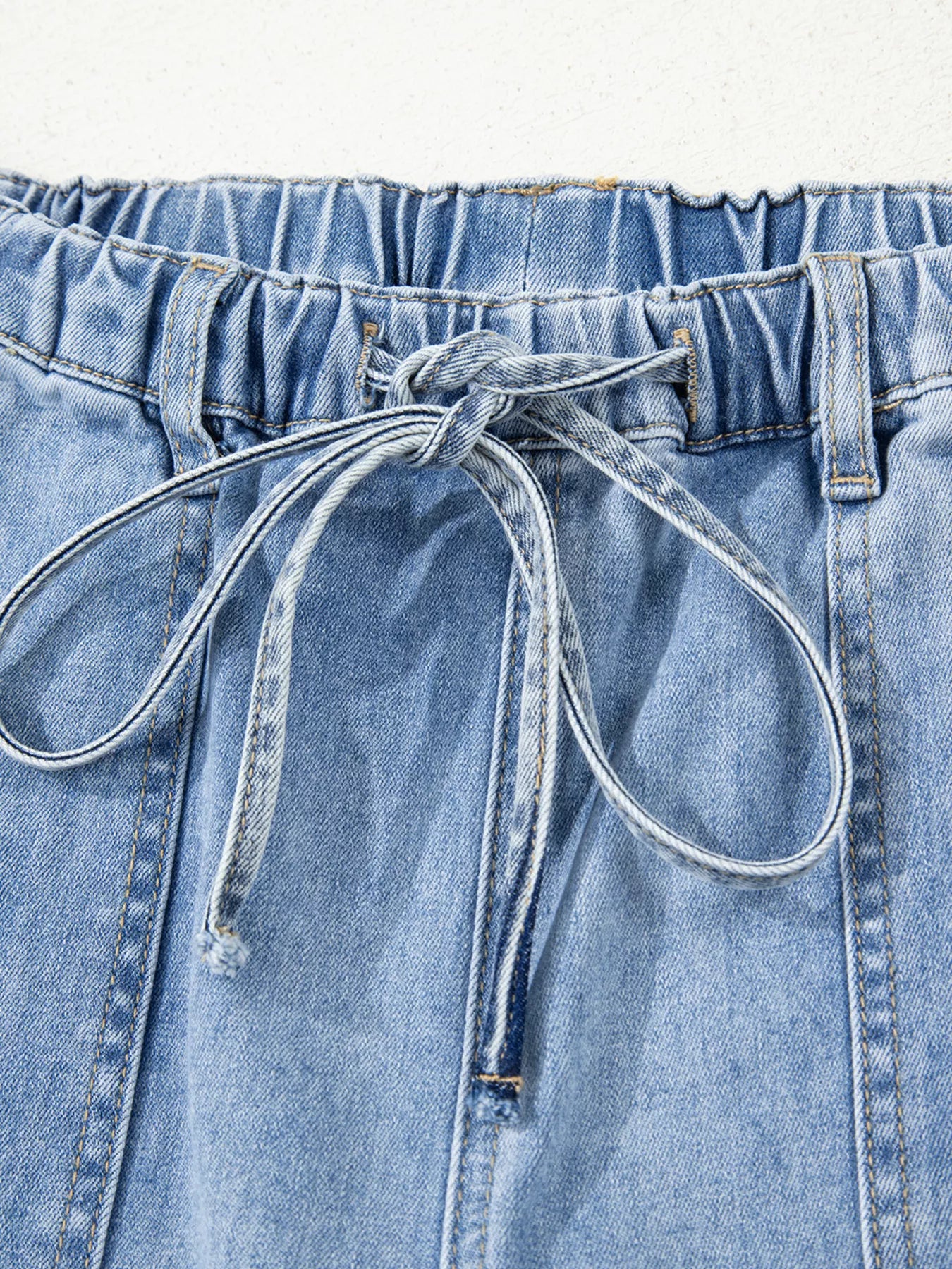 Close-up of light wash wide-leg jeans with drawstring waist and raw hem.