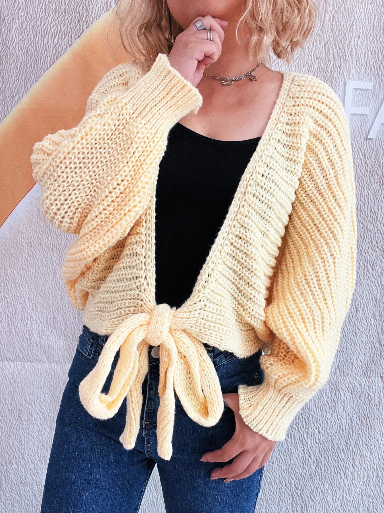 Light blue tie-front long sleeve knit cardigan worn open over a black top and jeans.