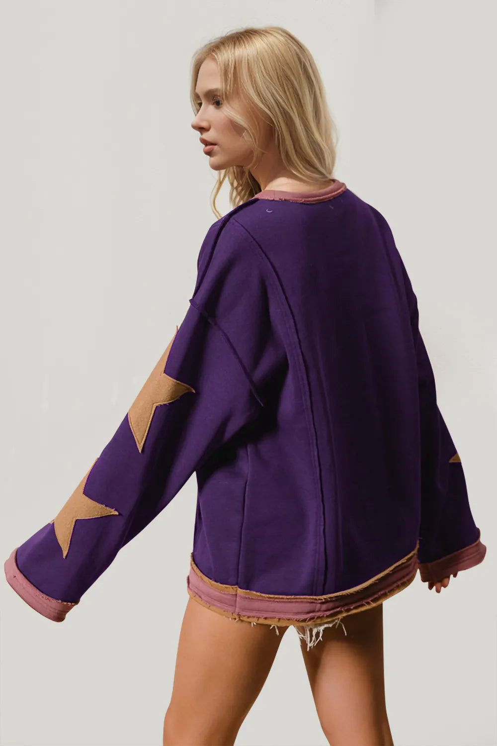 Purple long sleeve sweatshirt with oversized star patches on sleeves, modeled from behind.
