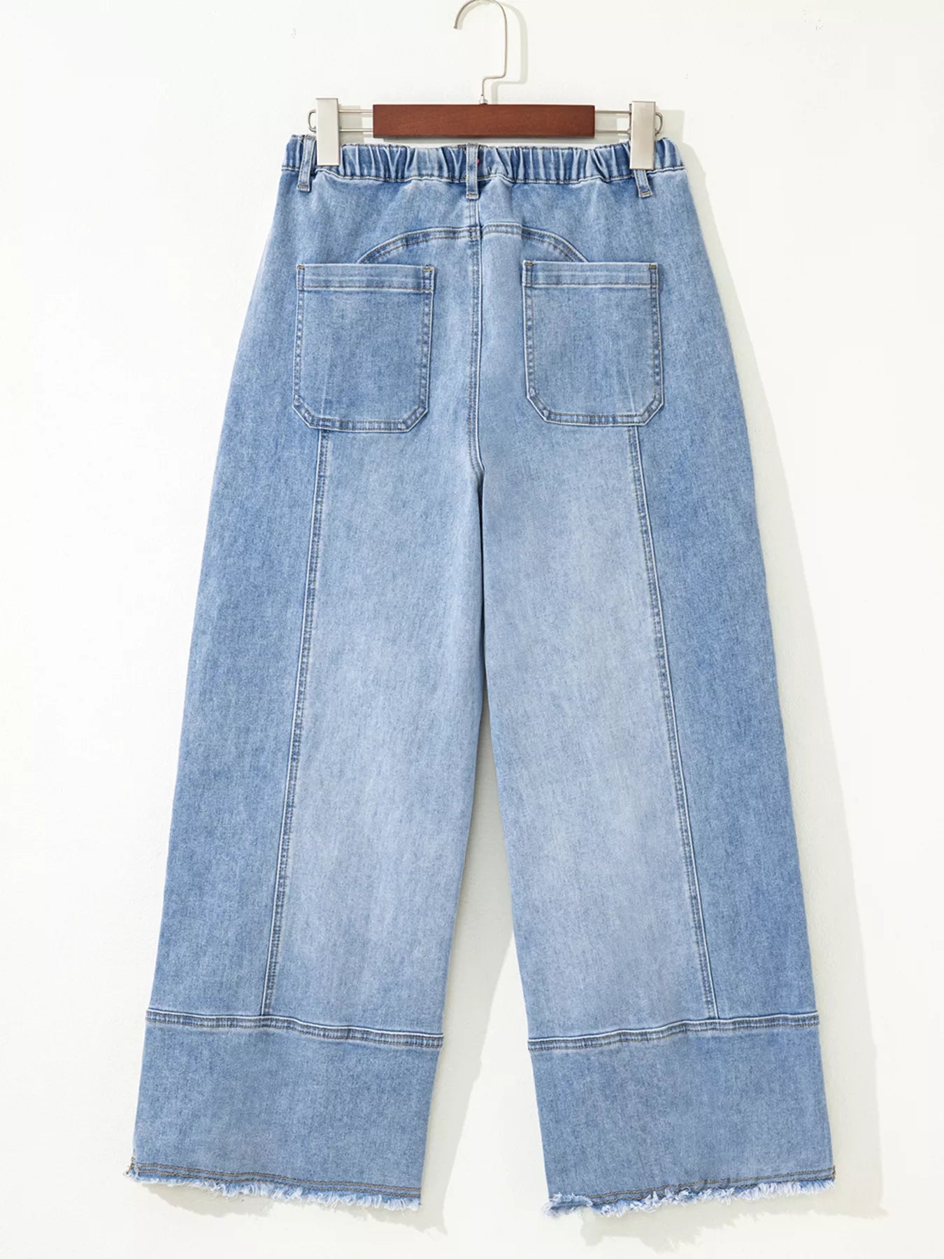 Rear view of light wash wide-leg jeans with drawstring waist and raw hem.