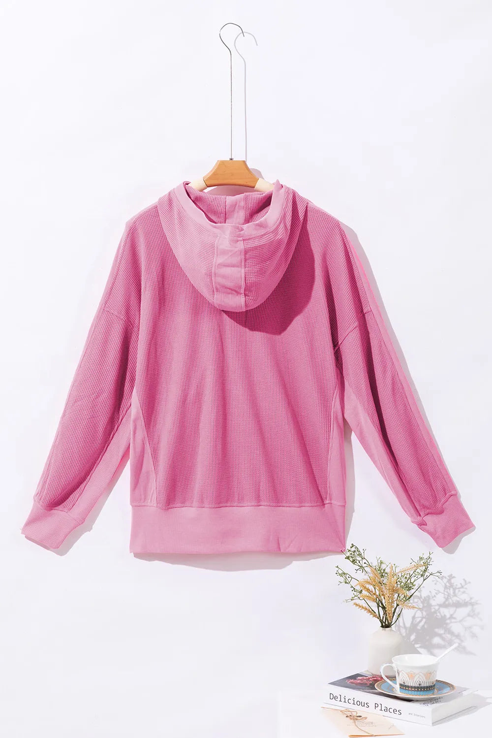 Back view of a soft pink waffle-knit zip-up hooded jacket on a hanger.