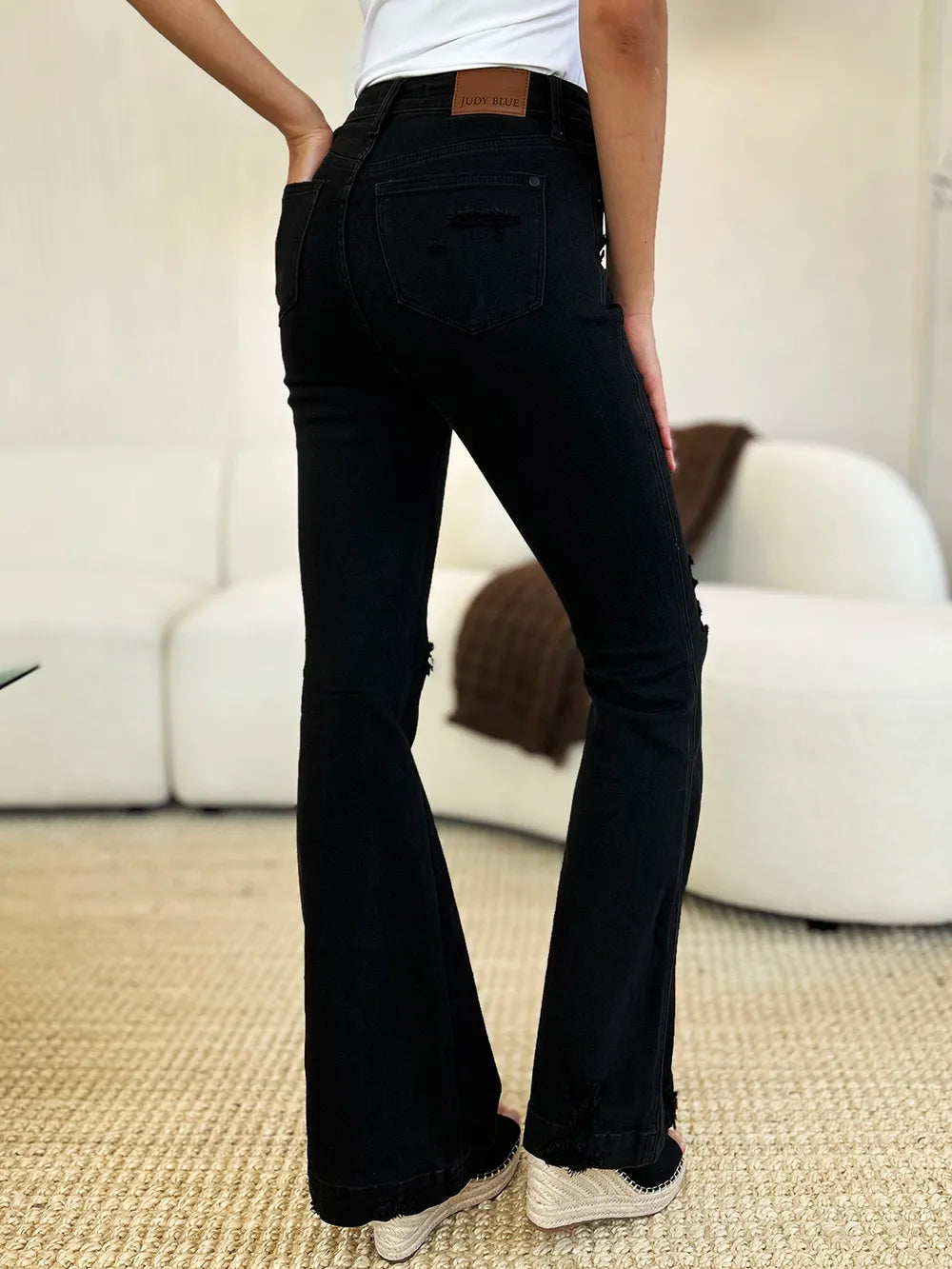 Side view of a model wearing black high-waist distressed flare jeans.