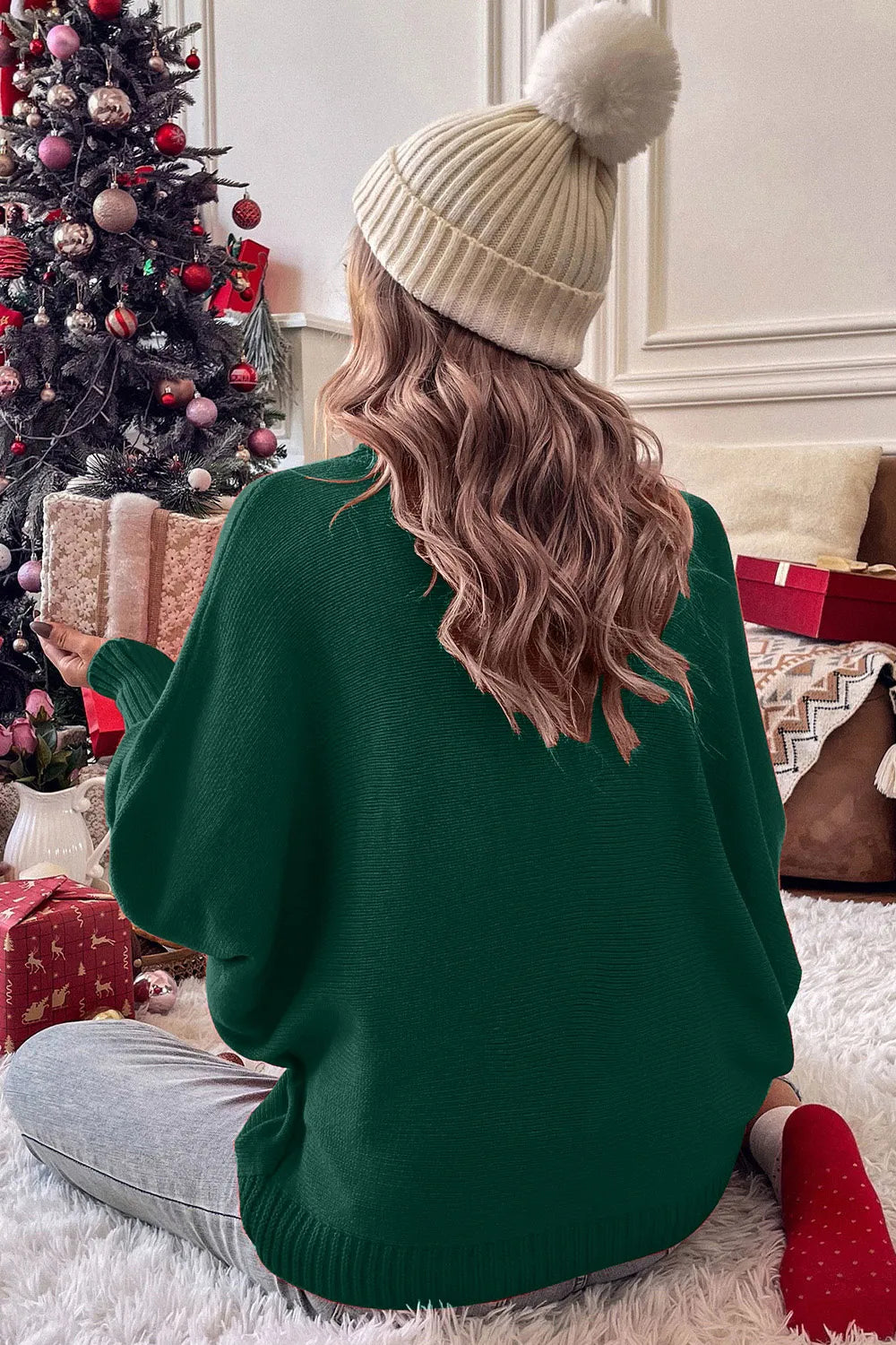 Back view of a woman wearing a green turtleneck sweater with bell sleeves in a festive room.