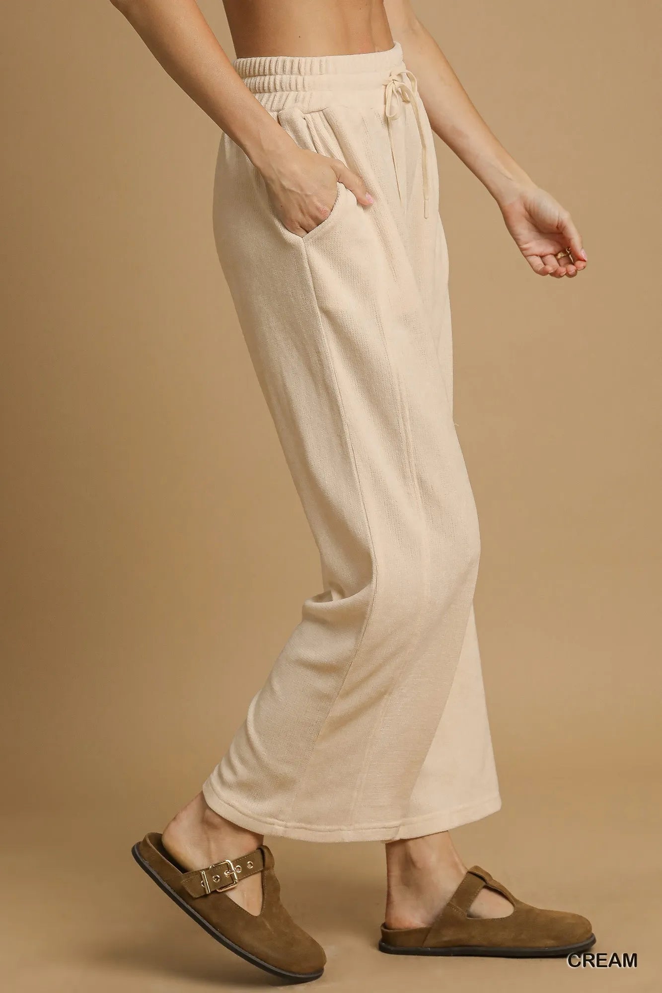 Cream drawstring wide-leg pants with flowy fit, modeled on a person walking.