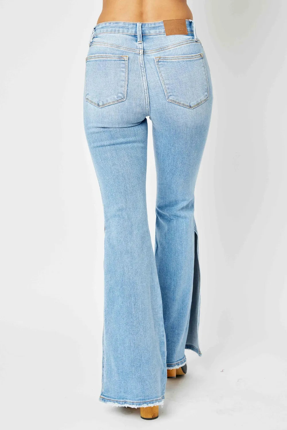 Rear view of light wash mid-rise raw hem flare jeans on a model.