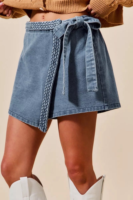 Blue denim wrap skort with braided trim and tie belt, styled with a cardigan and white boots.