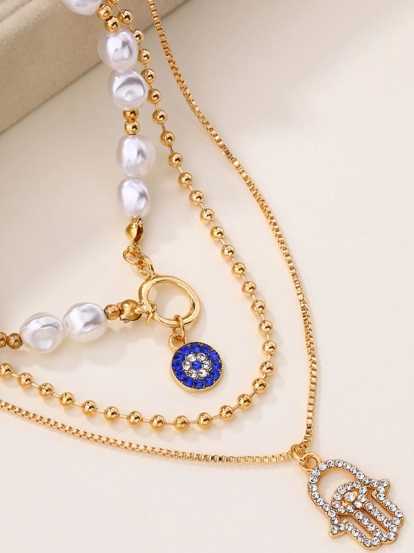 Layered 18K gold-plated necklace with pearls, blue evil eye, and hamsa pendant.