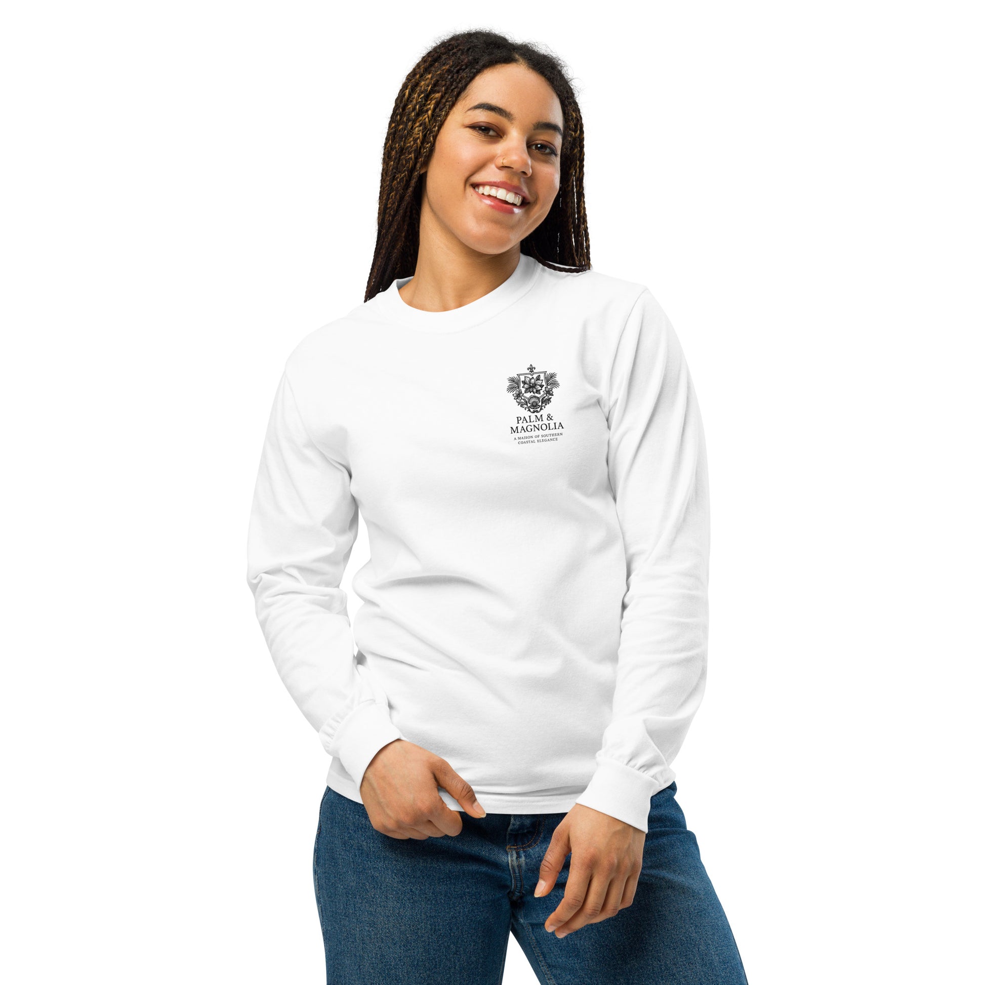 A smiling woman models a white unisex long-sleeve tee with a Harvest by the Pier palm and magnolia print on the chest.
