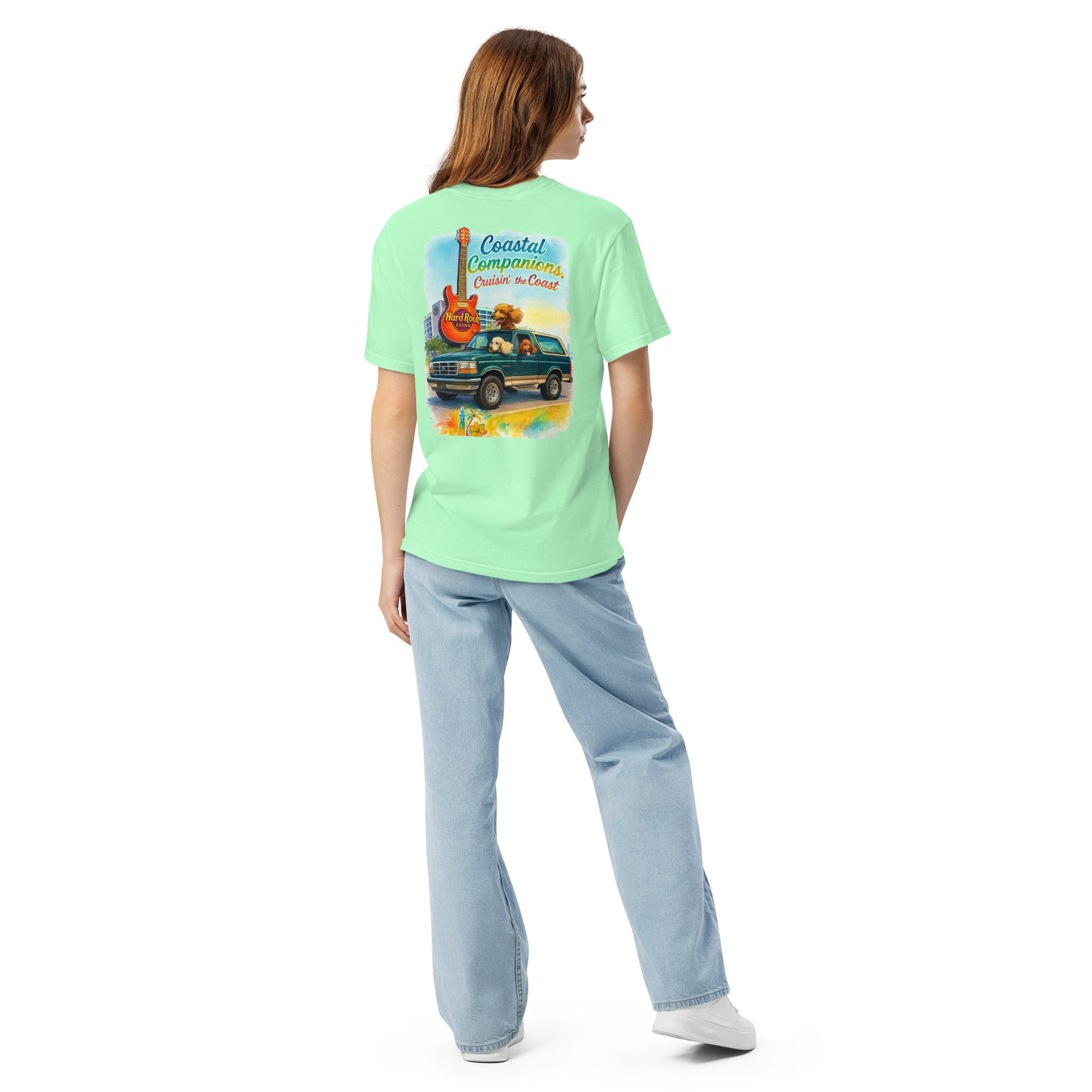 Back view of a woman wearing a light green short-sleeve tee with a coastal design featuring a guitar, truck, and dog.