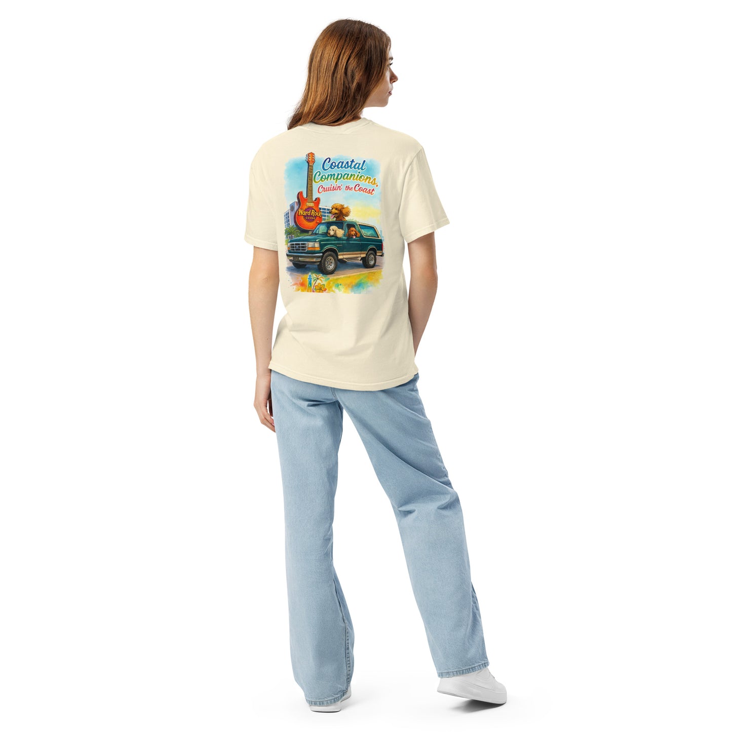 Back view of a woman wearing a cream Comfort Colors tee with a coastal design featuring a green Bronco, guitar, and dogs.