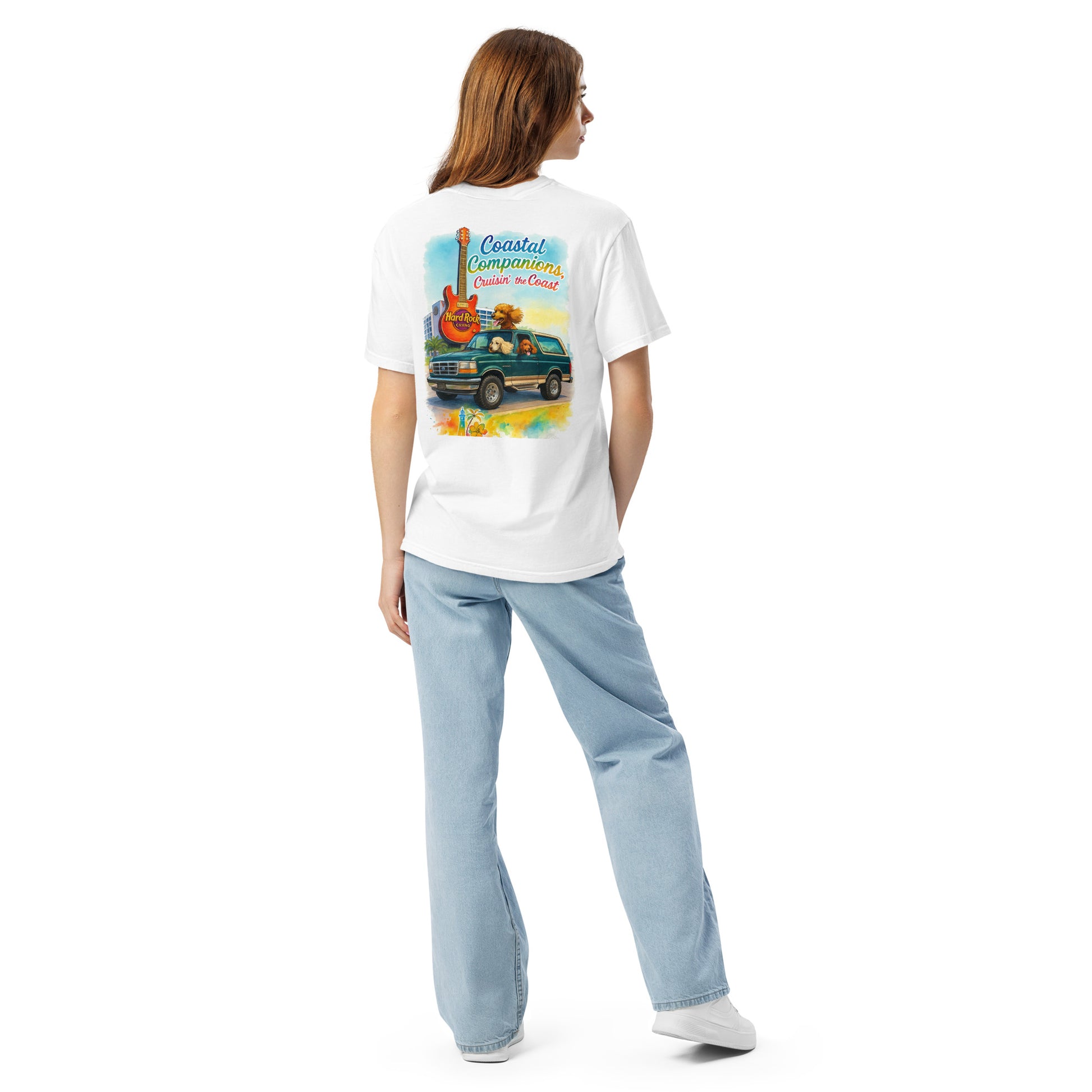 Back view of a woman wearing a white short-sleeve tee with a colorful coastal design featuring a green Bronco and guitar.