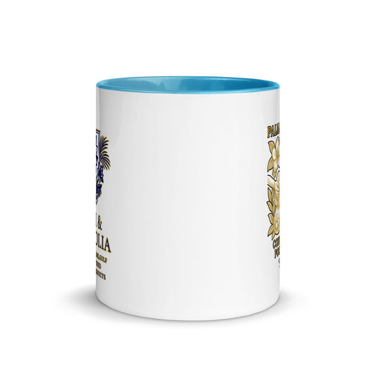 White ceramic mug with blue rim, navy Palm & Magnolia crest, and yellow accents.