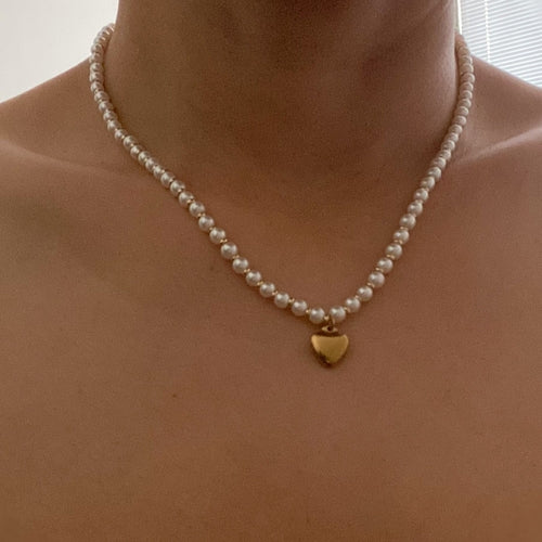 A necklace with alternating white pearls and gold beads, featuring a gold heart pendant.