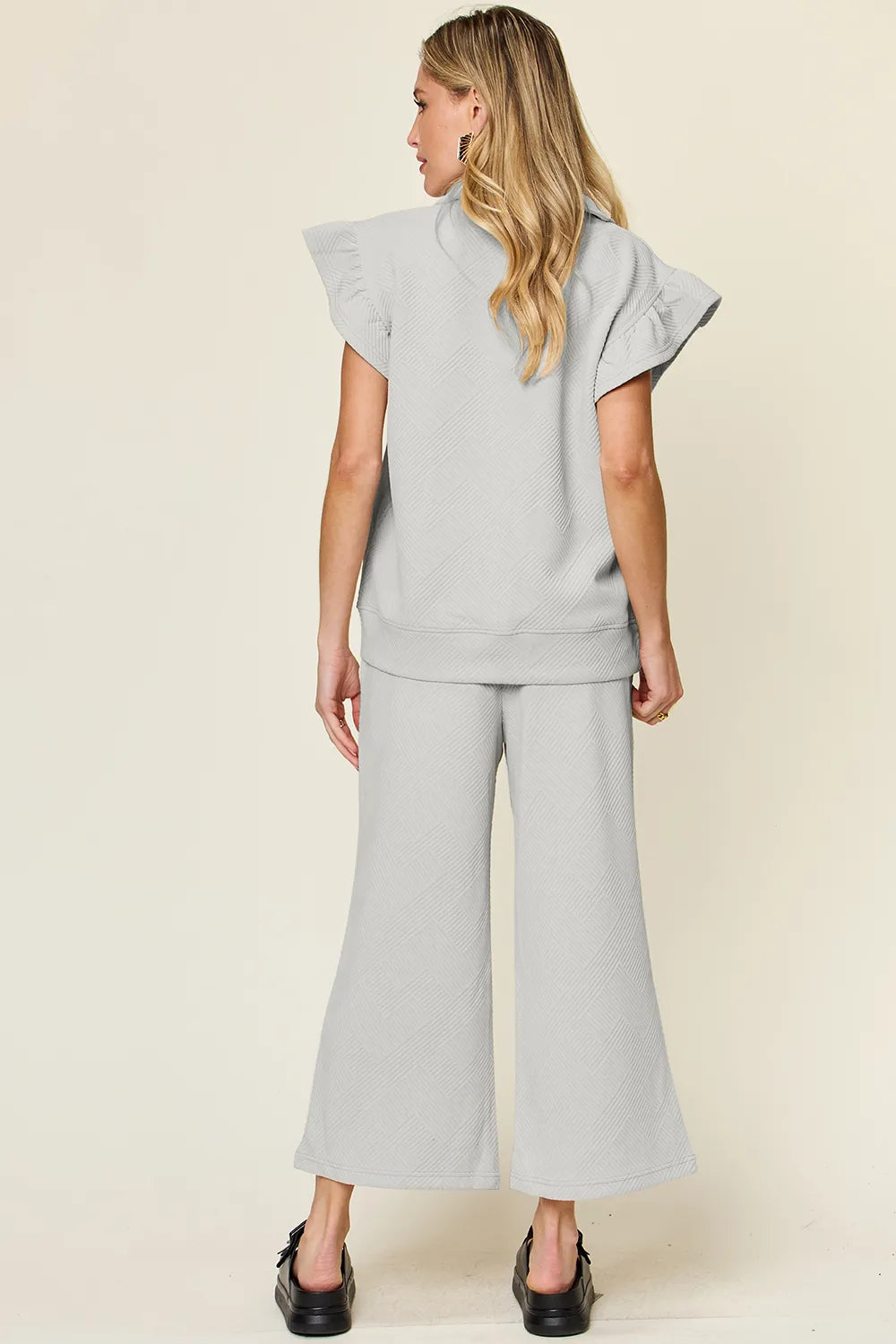 Rear view of a woman wearing a textured ruffle short sleeve top and wide leg pants set in gray.