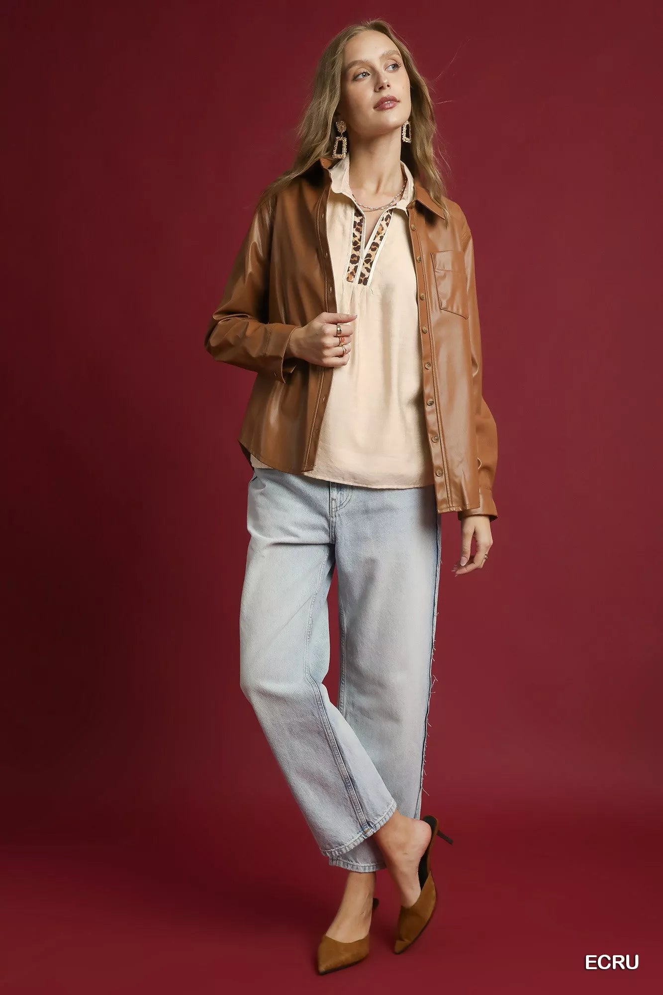 Woman wearing a long sleeve blouse with leopard print trim, paired with a tan jacket, light jeans, and nude heels.