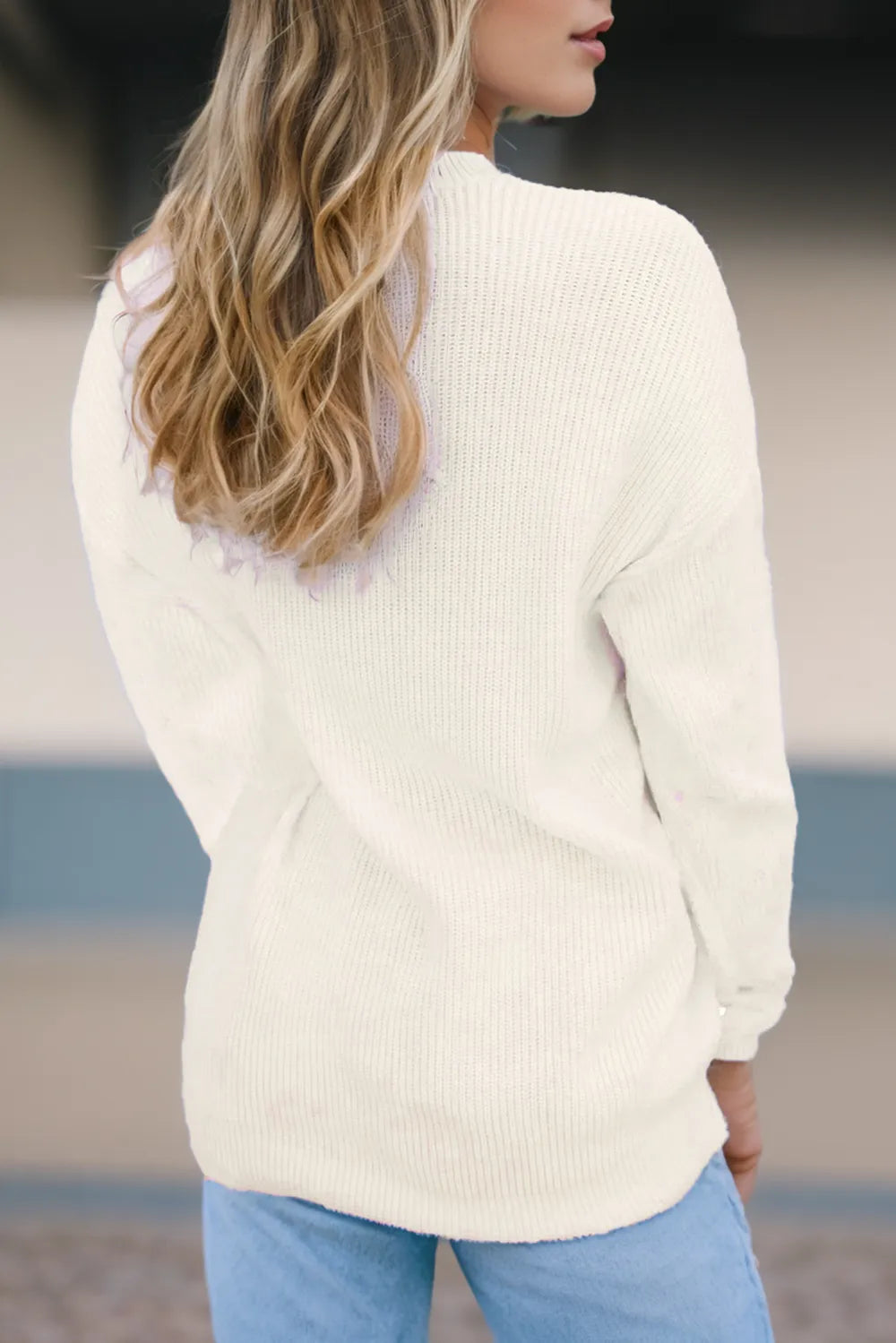 Rear view of a cream round neck sweater on a model with long blonde hair.
