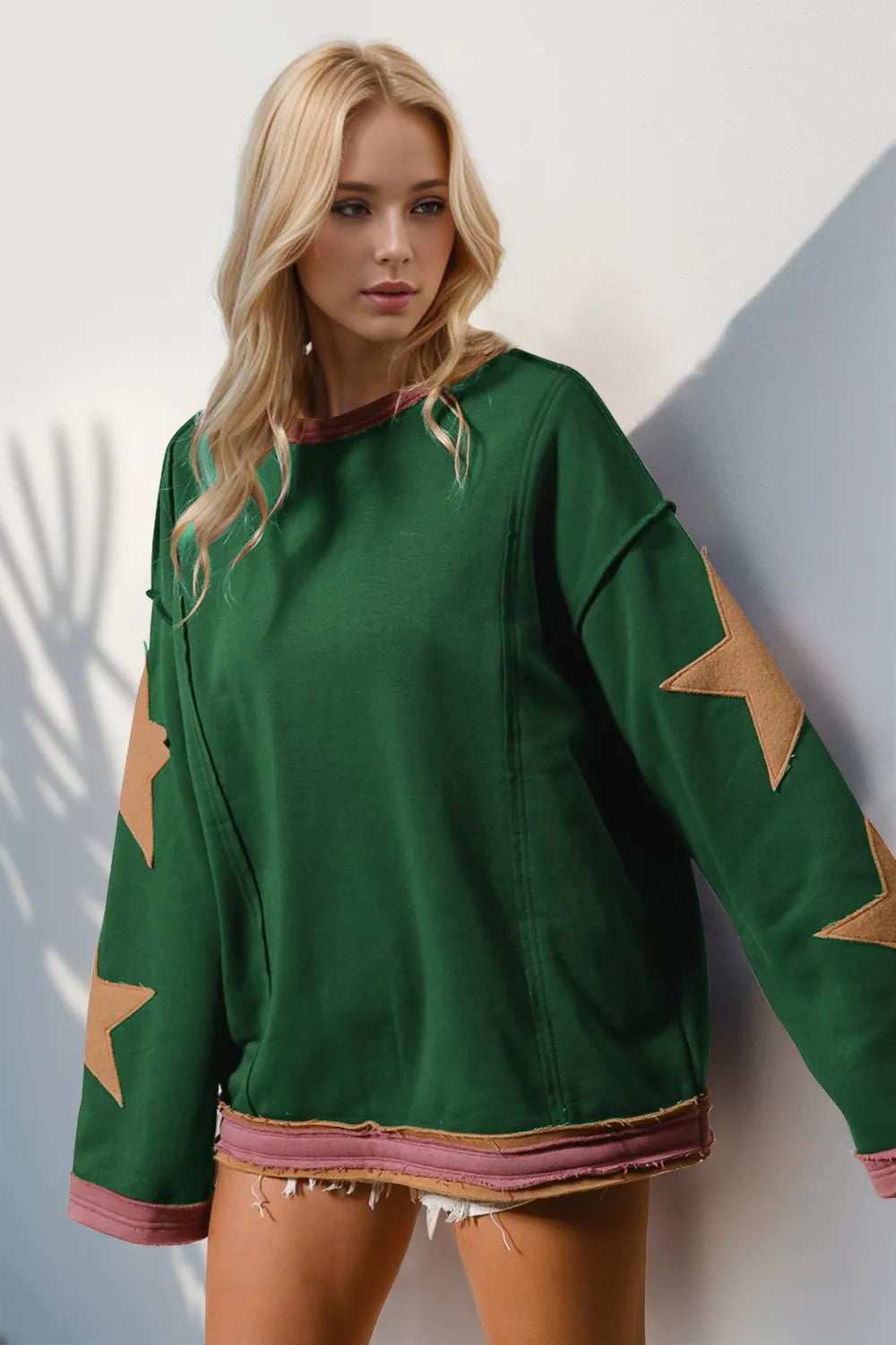 Green long-sleeve sweatshirt with oversized tan star patches on sleeves and exposed seams.