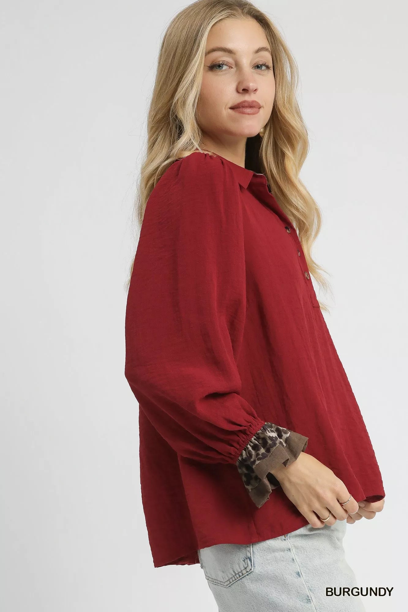 Woman modeling burgundy half-button blouse with leopard print cuffs and neckline.