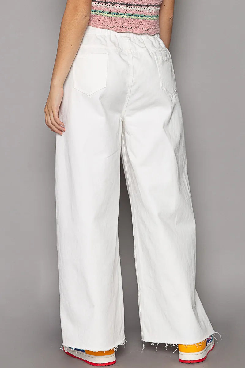 Rear view of white distressed drawstring wide-leg cotton pants with frayed hems.