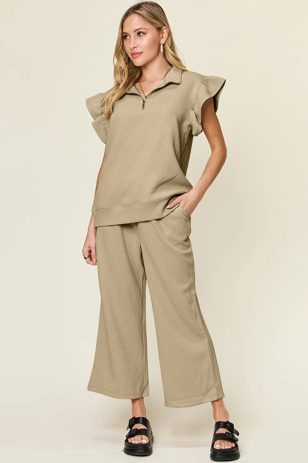 Woman modeling a textured ruffle short sleeve top with zipper and wide leg pants set in khaki.