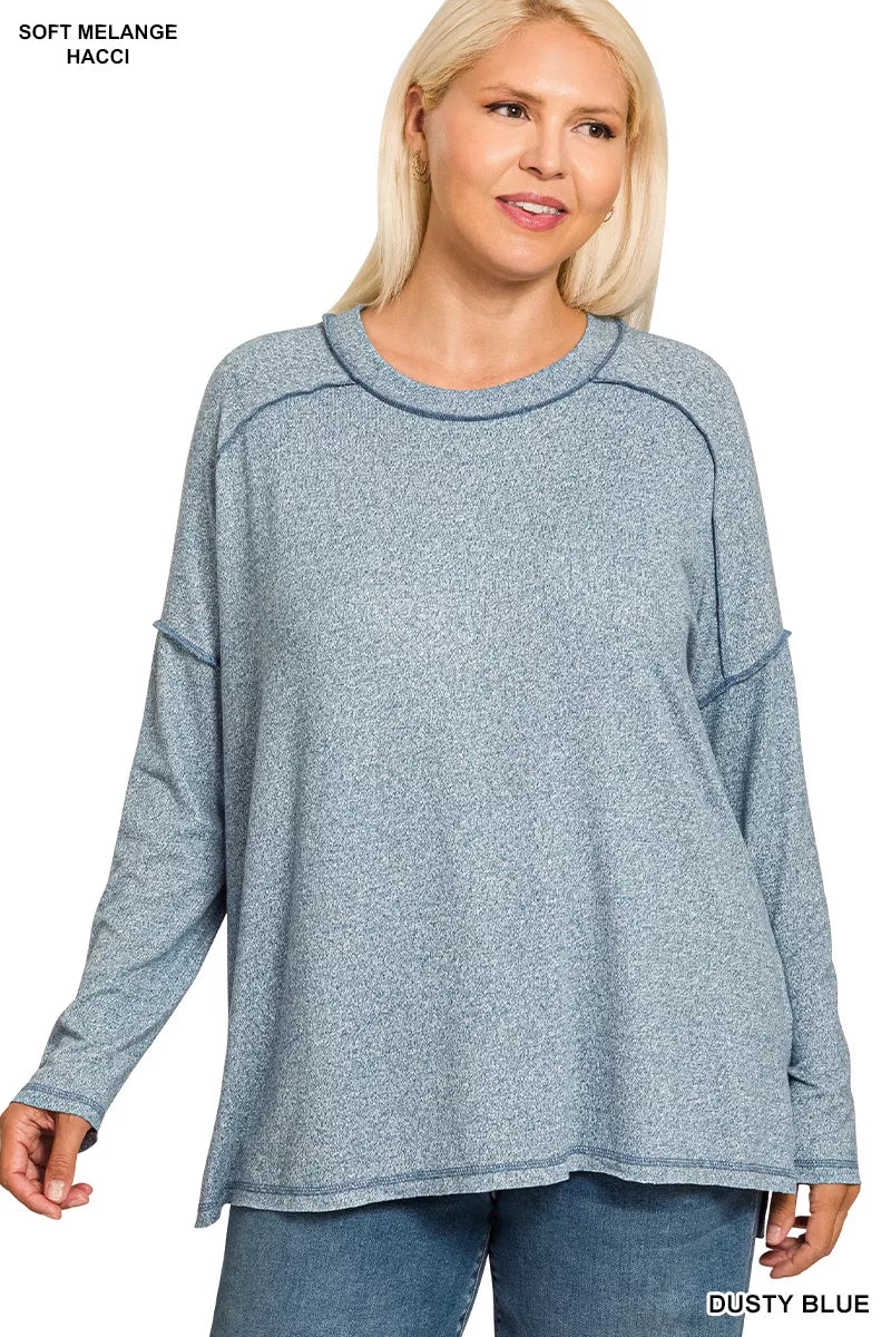 Woman modeling a dusty blue melange hacci exposed seam hi-low tee with long sleeves.