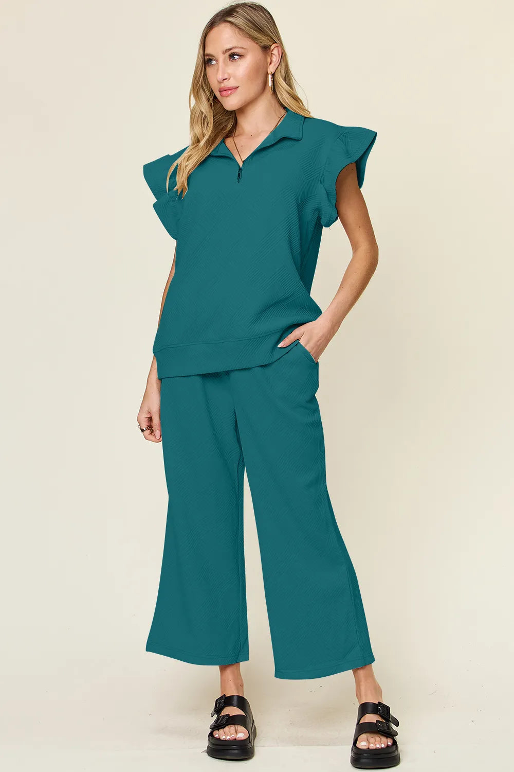 Woman modeling a textured teal ruffle short sleeve top and wide leg pants set.